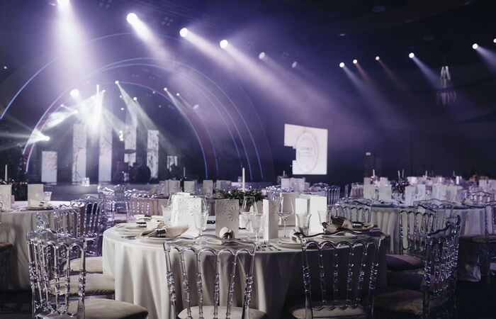 elegant geschmückte Tische für eine Abendveranstaltung mit Bühne im Hintergrund