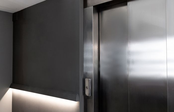Atmosphärisches Bild einer geschlossenen Aufzugtür mit Knopf und einer Beleuchtung neben dem Aufzug