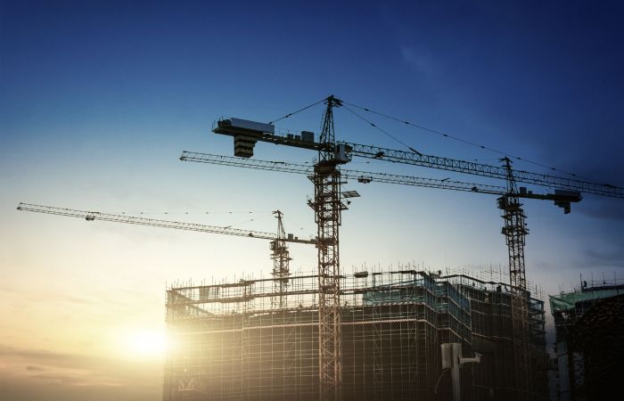 Baustelle eines Bürogebäudes am frühen Abend mit untergehender Sonne und mehreren Baukränen
