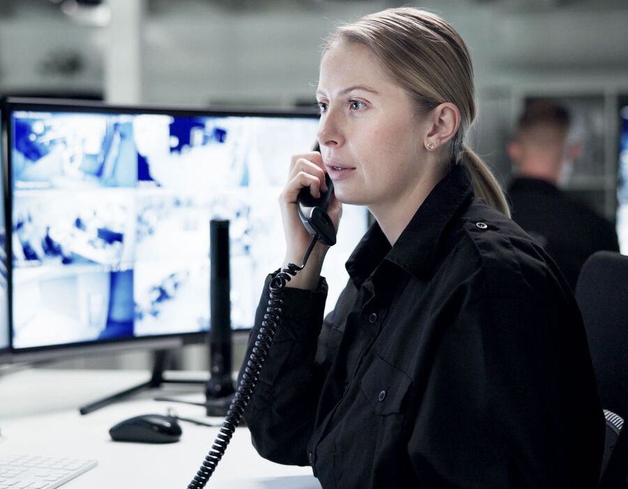 Mitarbeiterin eines Sicherheitsdiensts schaut konzentriert auf die Überwachungsmonitore während sie telefoniert