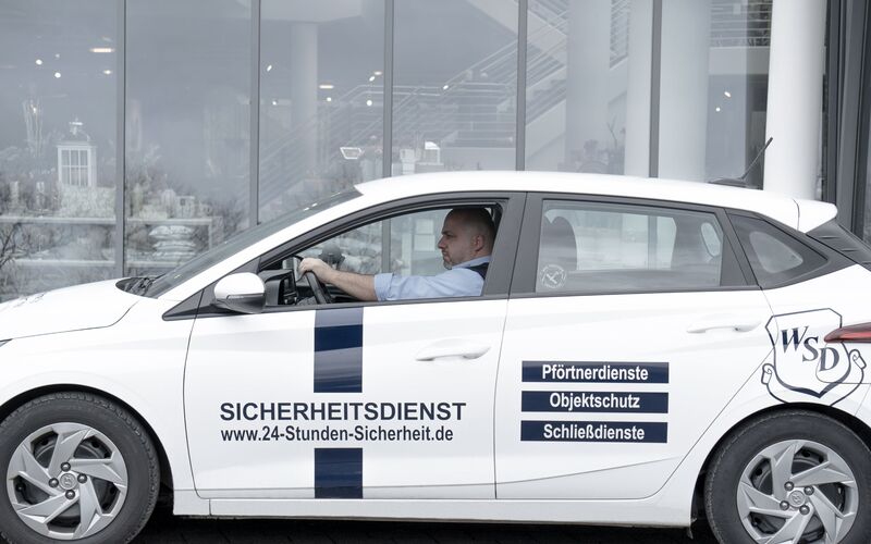 Sicherheitsmitarbeiter fährt in einem Auto vor einem Gebäude entlang
