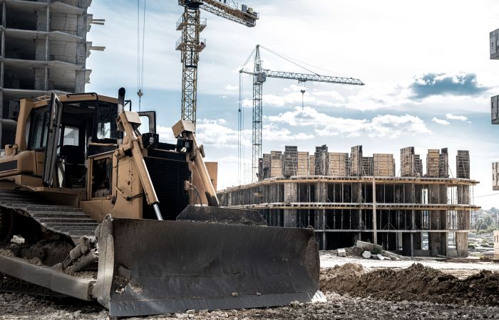 Baustelle eines Bürogebäudes mit einem Bagger im Vordergrund und großen Baukränen im Hintergrund