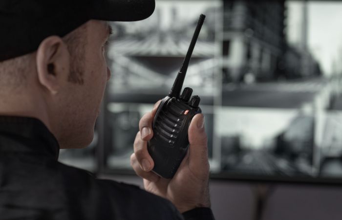 männlicher Sicherheitsmitarbeiter spricht in einen Sprechfunk und betrachtet Überwachungsmonitore