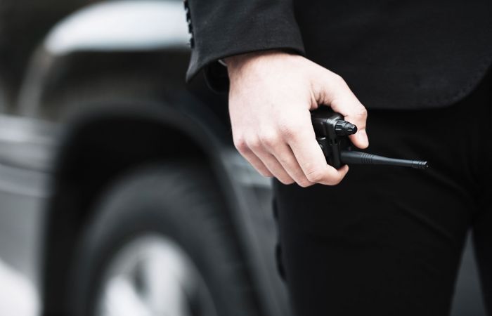 Sicherheitsmitarbeiter mit Sprechfunk in der Hand und einem Auto im Hintergrund
