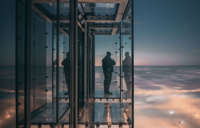 Außenaufnahme eines modernen Aufzugs aus Glas, der sich an der Außenseite eines hohen Glasgebäudes befindet, weit über der beleuchteten Stadt