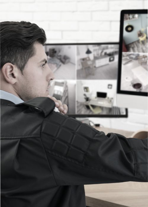 Sicherheitsmitarbeiter mit schwarzer Kleidung schaut konzentriert auf Überwachungsbildschirme