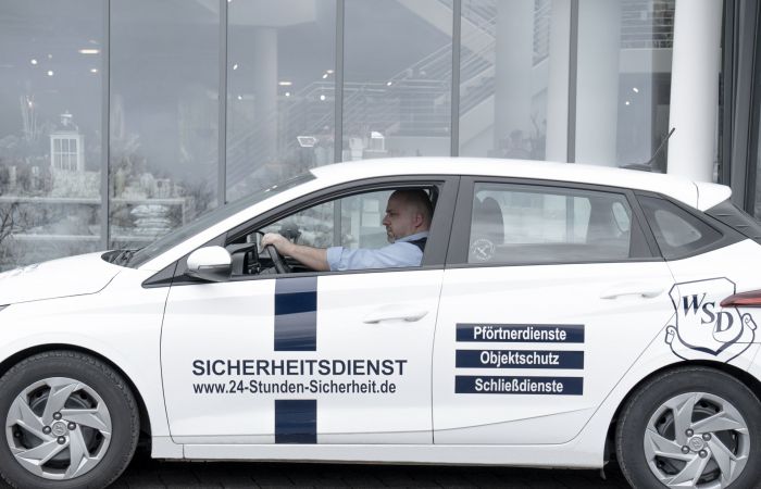 Sicherheitsmitarbeiter fährt in einem Auto vor einem Gebäude entlang