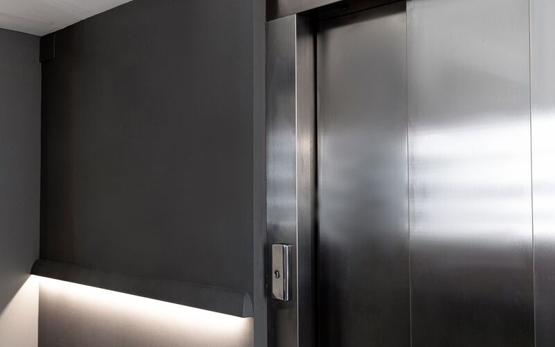 Atmosphärisches Bild einer geschlossenen Aufzugtür mit Knopf und einer Beleuchtung neben dem Aufzug