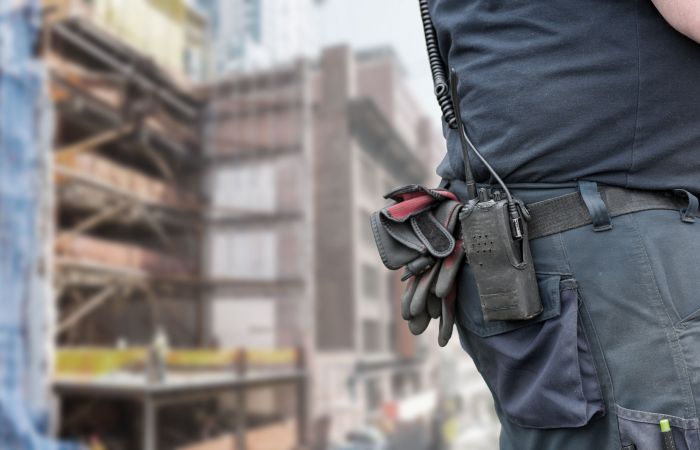 Ausschnitt eines Bauarbeiters, im Hintergrund ist die Baustelle eines Bürogebäudes zu sehen