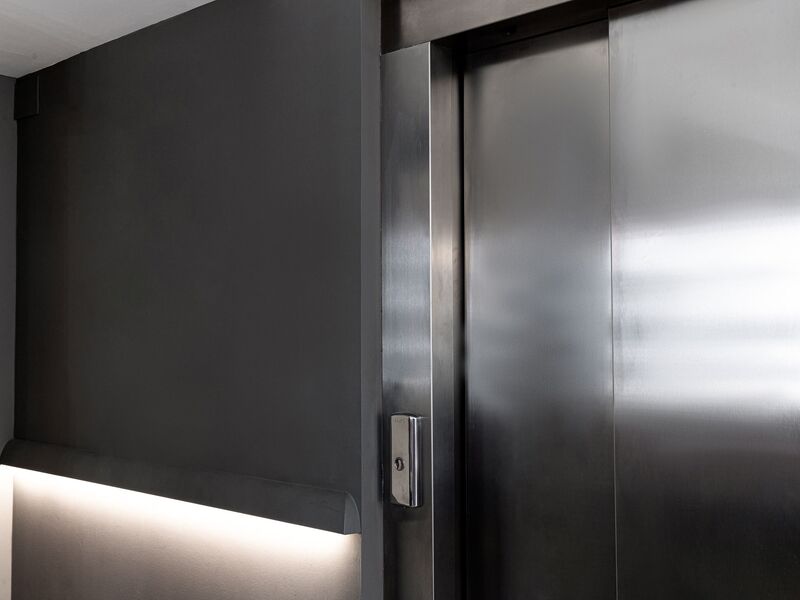 Atmosphärisches Bild einer geschlossenen Aufzugtür mit Knopf und einer Beleuchtung neben dem Aufzug