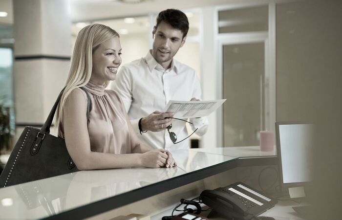 Geschäftsfrau steht lächelnd am Empfang und spricht mit dem freundlichen Pförtner