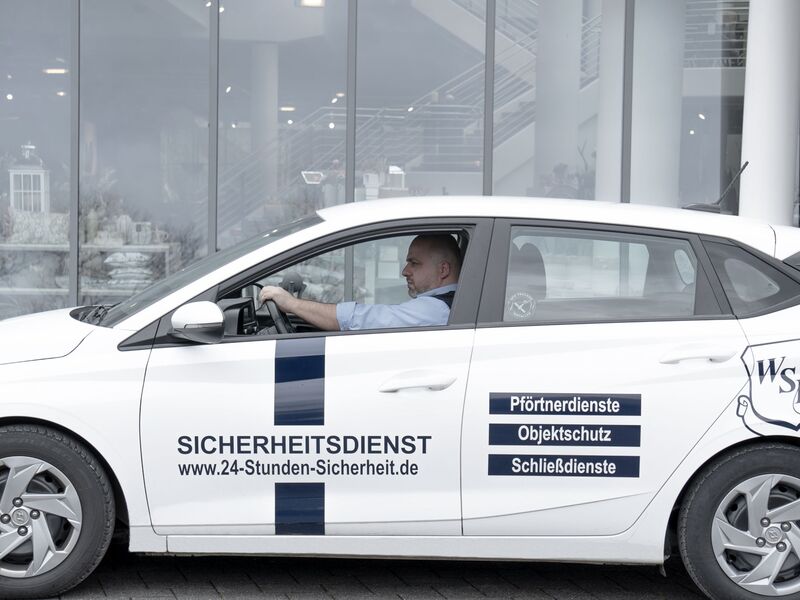 Sicherheitsmitarbeiter fährt in einem Auto vor einem Gebäude entlang