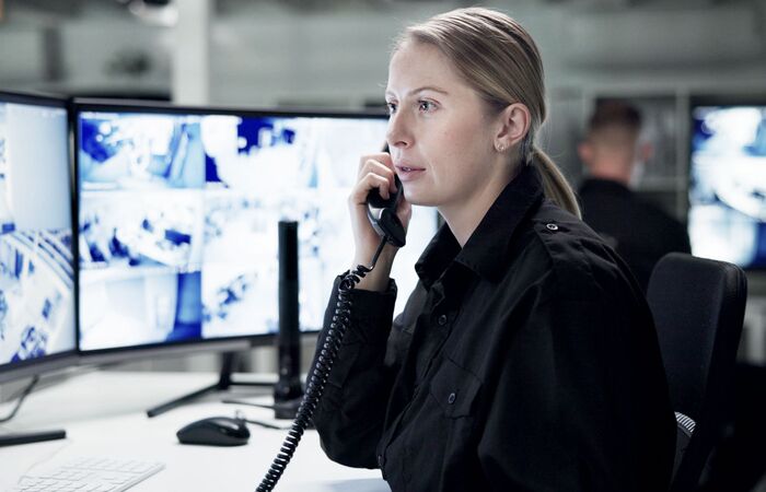 Mitarbeiterin eines Sicherheitsdiensts schaut konzentriert auf die Überwachungsmonitore während sie telefoniert