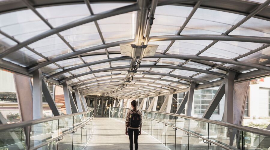 moderner Heller Durchgang, mit Glas überdacht, durch den eine junge Frau mit Rucksack geht