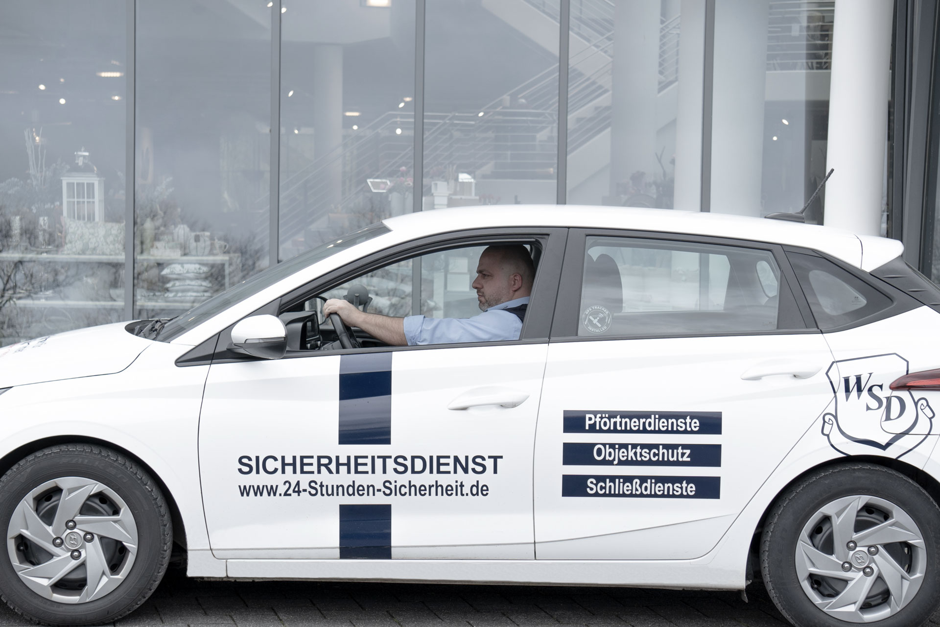 Sicherheitsmitarbeiter fährt in einem Auto vor einem Gebäude entlang